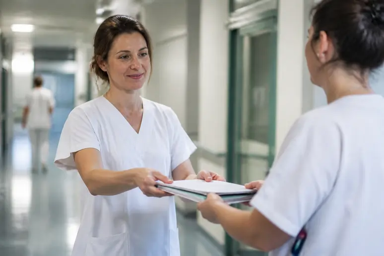En France, une brancardière expérimentée discute d'un dossier patient avec une collègue dans un hôpital, illustrant le salaire brancardier.