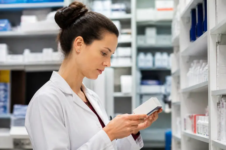Un pharmacien analyse une boîte de médicaments, illustrant l'impact sur le pouvoir d'achat des IADE.